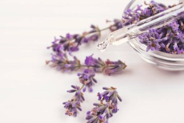 Etrafında lavanta yağı ve lavanta çiçekleri olan damlacıkların beyaz arka planda fotokopi ile yakın görüntüsü. Güzellik tedavileri ve aromaterapi konsepti. Seçici odak