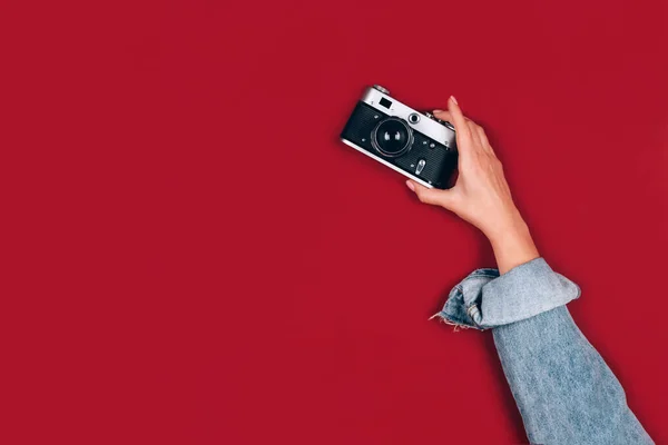 Female hand holding old retro photo camera on red background with copy space for text. Trendy vintage photography, Online photography school concept. Selective focus — Stock Photo, Image