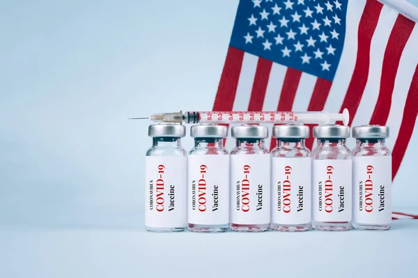 COVID-19 vaccine vials against USA flag on blue background with copy space for text - coronavirus vaccine doses, USA vaccination concept. Selective focus