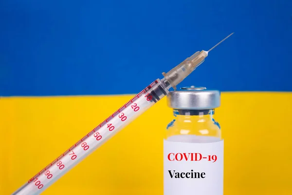 COVID-19 вакцина флакон проти українського прапора на синьому тлі з копіювальним простором для тексту - дози вакцини від коронавірусу, вакцинації в українській концепції. Вибіркове зосередження — стокове фото