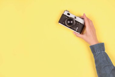 Gri ve sarı renkli modaya uygun kompozisyon, 2021 yılının rengi - kadın eli fotokopi alanı ile sarı zemin üzerinde retro fotoğraf makinesini tutuyor. Çevrimiçi fotoğrafçılık okulu konsepti, seçici odak