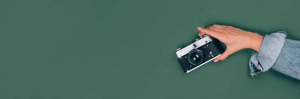 Yeşil arka planda eski model fotoğraf makinesini tutan kadın eli afişi ve metin için fotokopi alanı. Moda vintage fotoğrafçılık, çevrimiçi fotoğrafçılık okulu konsepti, seçici odak