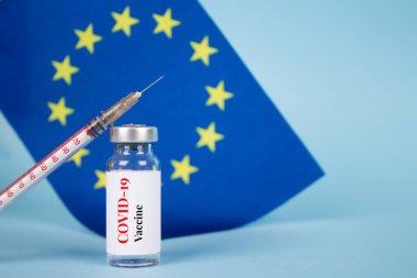 Mavi zemin üzerinde AB bayrağına karşı COVID-19 aşı şişesi ve metin için fotokopi alanı - koronavirüs aşısı dozları, Avrupa aşı konsepti, seçici odaklanma