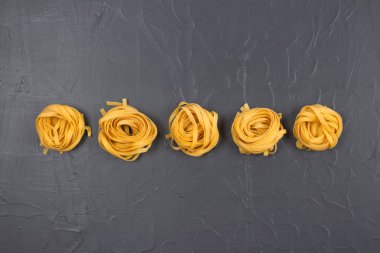 Ev yapımı tagliatelle yuvalarının üst görüntüsü, gri taştan arka planda fotokopi alanı olan sarı makarna. 2021 yılının renkli İtalyan yemekleri. Taze ev yapımı ya da yarı pişmiş yiyecek. Seçici odak