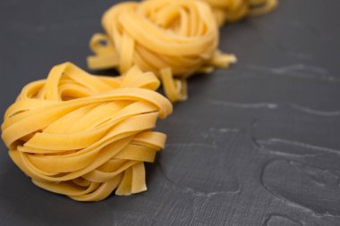 Ev yapımı tagliatelle yuvaları, gri taştan arka planda fotokopi alanı olan sarı makarna. 2021 yılının renkli İtalyan yemekleri. Taze ev yapımı ya da yarı pişmiş yiyecek. Seçici odak