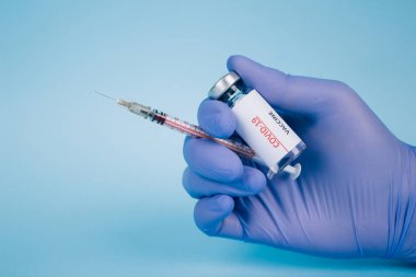 Doktor ya da bilim adamı elinde COVID-19 aşısı bulunan mavi arkaplandaki şırıngayla metin için fotokopi alanı tutuyor. Koronavirüsü önleme, küresel aşı kavramı. Seçici odak