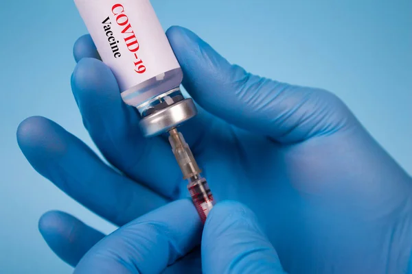 Doctor injecting with vial dose of COVID-19 vaccine with syringe against blue background with copy space - prevention coronavirus, global vaccination concept. Selective focus — Stock Photo, Image