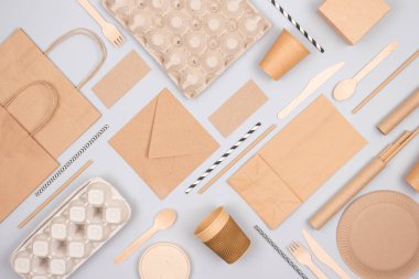 Gri arka planda çevre dostu sofra takımı ve kraft kağıt gıda ambalajlı düz kompozisyon. Sürdürülebilir ambalaj, geri dönüşümlü kağıt takımı, sıfır atık ambalaj konsepti. Model, seçici odak