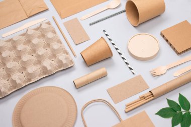 Açık gri arka planda çevre dostu sofra takımı ve Kraft kağıt gıda ambalajı. Sokak yiyecekleri ambalajı, fincanlar, tabaklar, pipetler, kaplar ve kese kağıtları. Model resim, düz uzanma