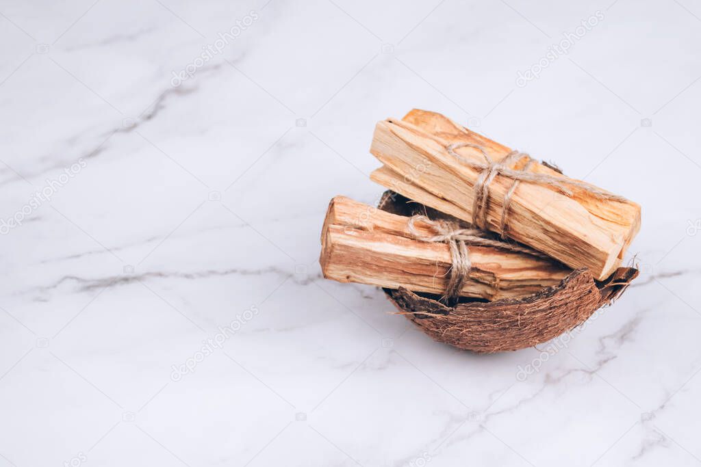 Palo Santo tree sticks inside coconut shell on marble background - holy incense tree from Latin America. Meditation, mental health and personal fulfilment concept. Selective focus