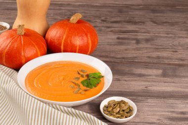 Beyaz kasede balkabağı kremalı çorba maydanozlu ve tahta masa arkasında kabak tohumlu metin için fotokopi alanı. Vejetaryen yemeği konsepti, ev yapımı çorba tarifi. Seçici odak