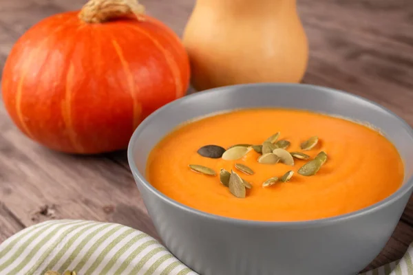 Hokkaido pumpkin cream soup in gray bowl toped with pumpkin seeds on wooden table background with copy space for text. Vegan food concept, homemade soup recipe. Selective focus