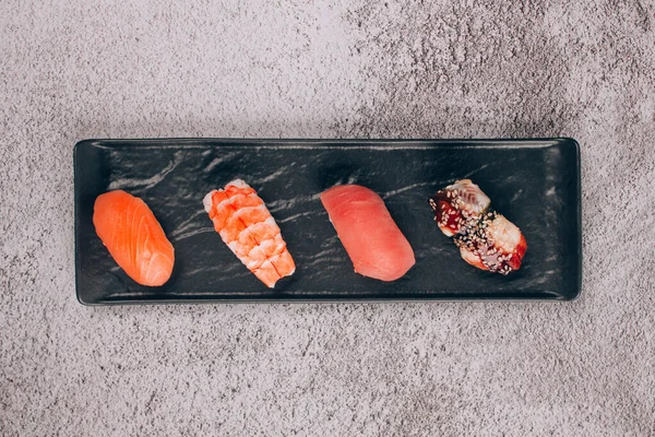 Набор традиционных японских нигири суши на черной тарелке на сером бетонном фоне - с сырым тунцом, лососиной рыбой, креветками и угрем. Концепция доставки азиатских блюд и суши-бара — стоковое фото