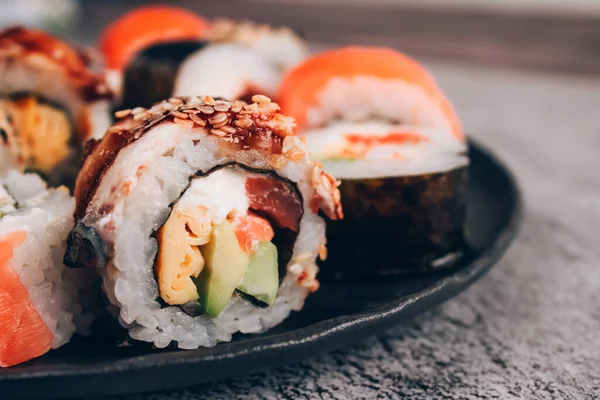 Sushi bar lunch menu. Closeup view of sushi rolls with salmon, avocado and smocked eel on the concrete table background - futomaki. uramaki, hosomaki. Order food online and home delivery food concept