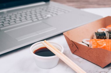 Farklı suşi rulolarını, beyaz mermer masa zemininde dizüstü bilgisayarı, futomaki, uramaki ve hosomaki ile servis kutusunda somon ile kapatın. Çevrimiçi sipariş gıda ve teslimat konsepti