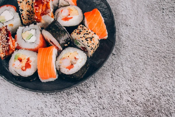 Sushi bar lunch menu. Top view of sushi rolls with salmon, avocado and smocked eel on the concrete table background with copy space. Order food online and home delivery food concept