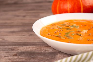 Kabak kremalı beyaz kasenin önü tahta masa arkasında balkabağı tohumları ve metin için fotokopi alanı ile kaplı. Vejetaryen yemeği konsepti, ev yapımı çorba tarifi. Sonbahar yemeği. Seçici odak