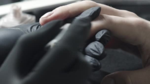 De meester in zwarte latex beschermende handschoenen dompelt een borstel in een buis met een beige vernis. Schoonheidssalon, Manicure — Stockvideo