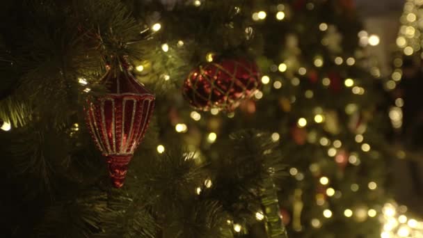 Close up of several red plastic Christmas toys hanging on an artificial Christmas tree. Stock video. Colorful decorations and garlands. Colored Christmas decorations. Bauble. Happy New Year. Vacation — Stock Video