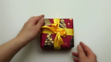 Yeni yıl hediyesinin yakın çekimi. Eller hediyeyi eline alır ve farklı açılardan inceler. Hediyeyi salla. Sarı kurdeleli yeni yıl paketleri. Kutu şenliği. Mutlu Noeller.