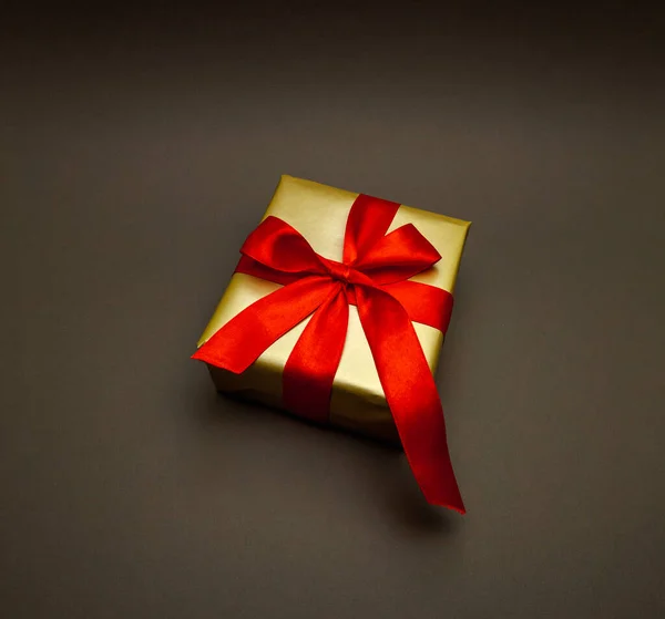 Dárek na dovolenou. Krabička ve zlatém dárkovém balení s červenou mašlí, na černém pozadí. Veselé Vánoce, Nový rok a Valentýn zdravím. Pohlednice — Stock fotografie