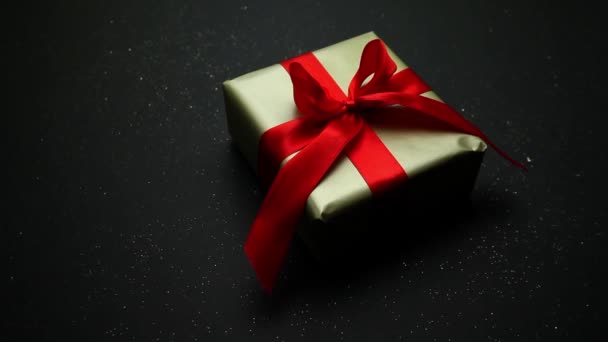 Festliches Geschenk in Goldverpackung und roter Schleife auf schwarzem Hintergrund. Ein angenehmes Geschenk und eine Überraschung für die Lieben. — Stockvideo