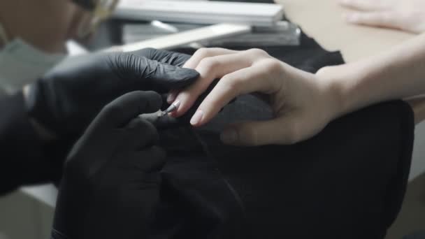 El maestro en guantes protectores de látex negro sumerge un cepillo en un tubo con un barniz beige. Salón de belleza, Manicura — Vídeo de stock