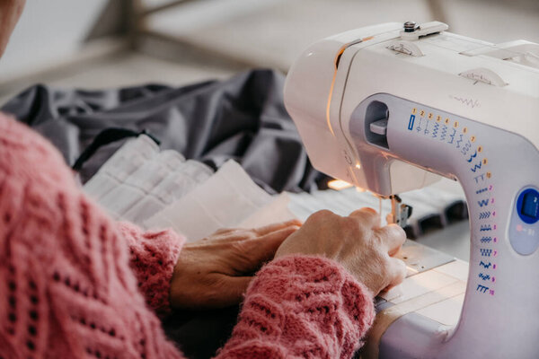 Close-up. The hands of an adult woman are sewing at a sewing machine. Manufacture of wearing apparel.