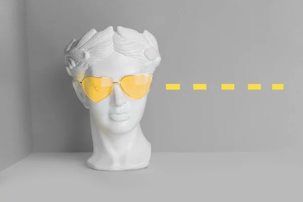 Hvid skulptur af et antikt hoved i gule briller med hjerter. På en geometrisk baggrund af to farver. Stock-billede