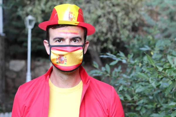 portrait of handsome young man in clothes colored in Spain flag and medical mask on nature