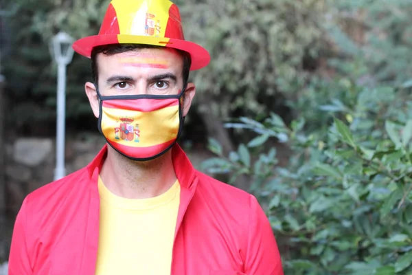 portrait of handsome young man in clothes colored in Spain flag and medical mask on nature