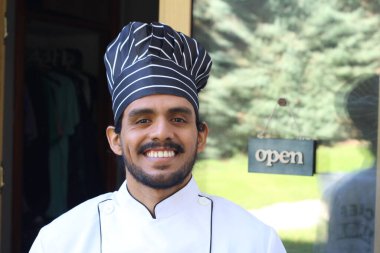 Yakışıklı Latin aşçının portresi. Üniformalı ve şapkalı. Restoran kapısının önünde.
