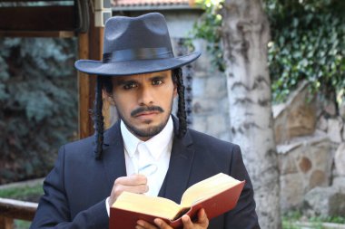 Geleneksel şapkalı yakışıklı hahamın doğal arka planda Tanakh ile yakın plan portresi.