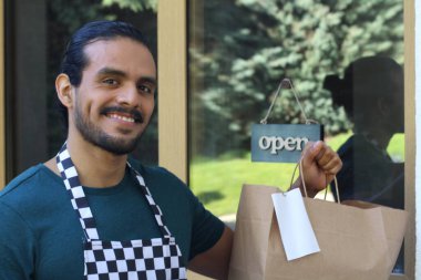 Kapının önünde kağıt torba ve açık hesap ile yakışıklı Latin üniformalı küçük işletme sahibi portresi