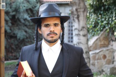 Geleneksel şapkalı yakışıklı hahamın doğal arka planda Tanakh ile yakın plan portresi.
