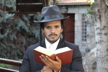Geleneksel şapkalı yakışıklı hahamın doğal arka planda Tanakh ile yakın plan portresi.
