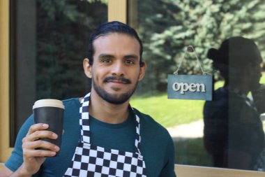 Kapının önünde kağıt kahve fincanı olan, üniformalı, yakışıklı, küçük işletme sahibinin portresi.