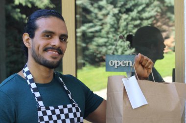 Kapının önünde kağıt torba ve açık hesap ile yakışıklı Latin üniformalı küçük işletme sahibi portresi