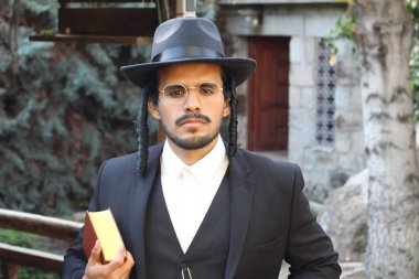 Geleneksel şapkalı yakışıklı hahamın doğal arka planda Tanakh ile yakın plan portresi.