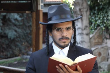 Geleneksel şapkalı yakışıklı hahamın doğal arka planda Tanakh ile yakın plan portresi.