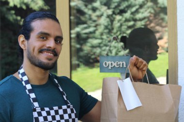 Kapının önünde kağıt torba ve açık hesap ile yakışıklı Latin üniformalı küçük işletme sahibi portresi