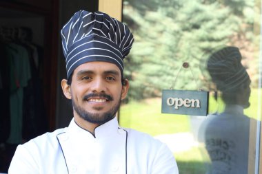 Yakışıklı Latin aşçının portresi. Üniformalı ve şapkalı. Restoran kapısının önünde.