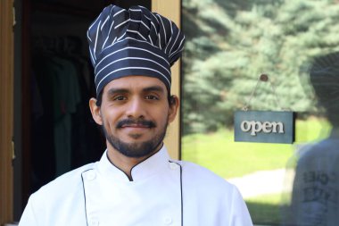 Yakışıklı Latin aşçının portresi. Üniformalı ve şapkalı. Restoran kapısının önünde.