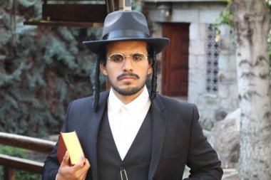 Geleneksel şapkalı yakışıklı hahamın doğal arka planda Tanakh ile yakın plan portresi.