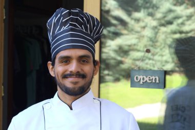 Yakışıklı Latin aşçının portresi. Üniformalı ve şapkalı. Restoran kapısının önünde.