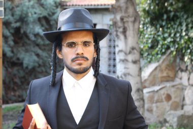 Geleneksel şapkalı yakışıklı hahamın doğal arka planda Tanakh ile yakın plan portresi.