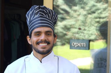 Yakışıklı Latin aşçının portresi. Üniformalı ve şapkalı. Restoran kapısının önünde.