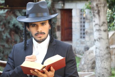 Geleneksel şapkalı yakışıklı hahamın doğal arka planda Tanakh ile yakın plan portresi.