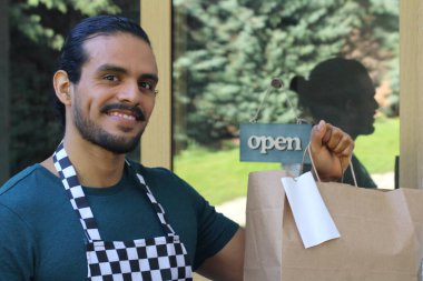 Kapının önünde kağıt torba ve açık hesap ile yakışıklı Latin üniformalı küçük işletme sahibi portresi