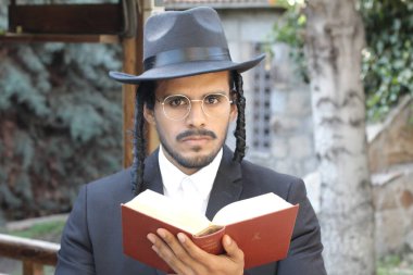 Geleneksel şapkalı yakışıklı hahamın doğal arka planda Tanakh ile yakın plan portresi.